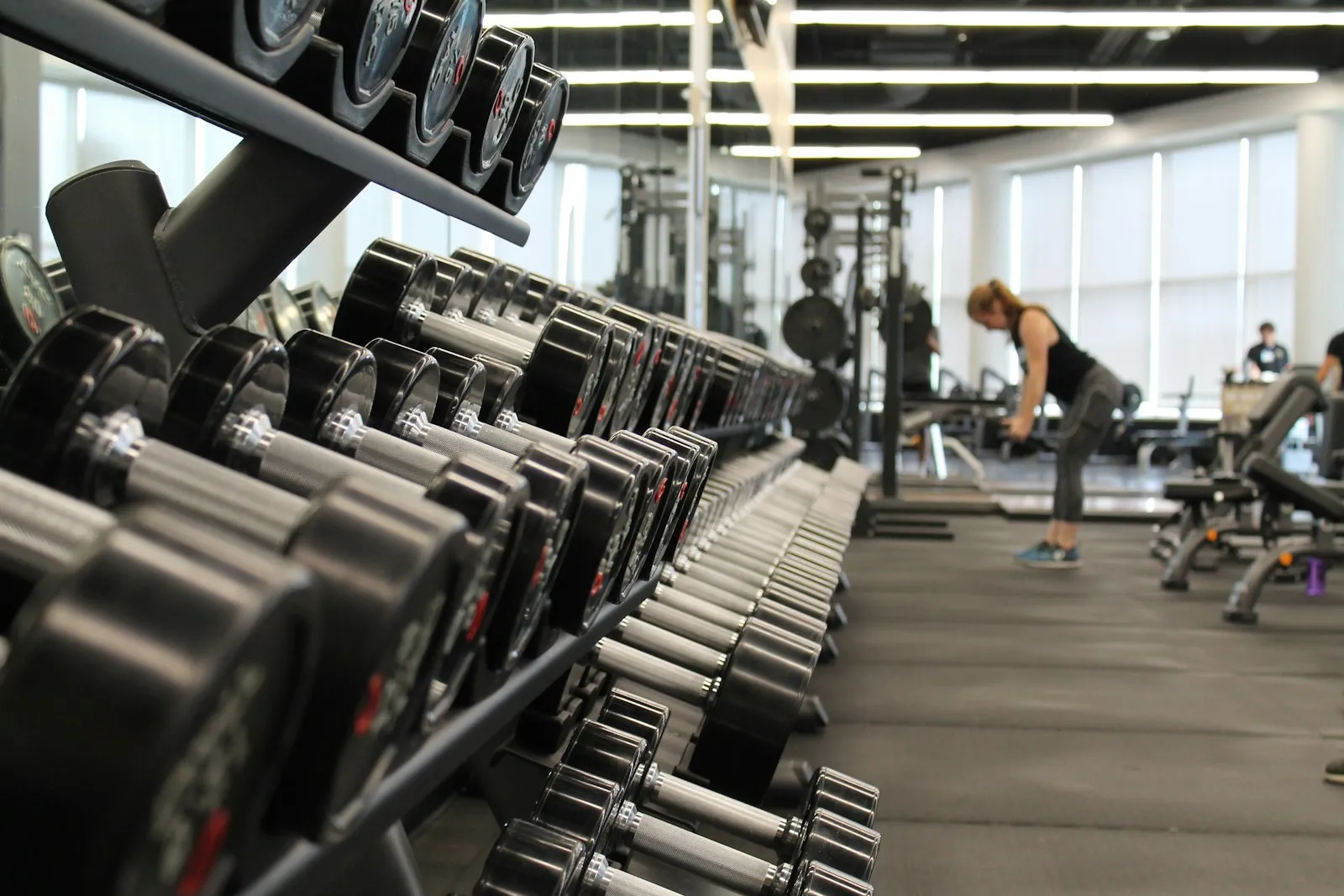 Gimnasio con mancuernas ordenadas y una persona entrenando al fondo